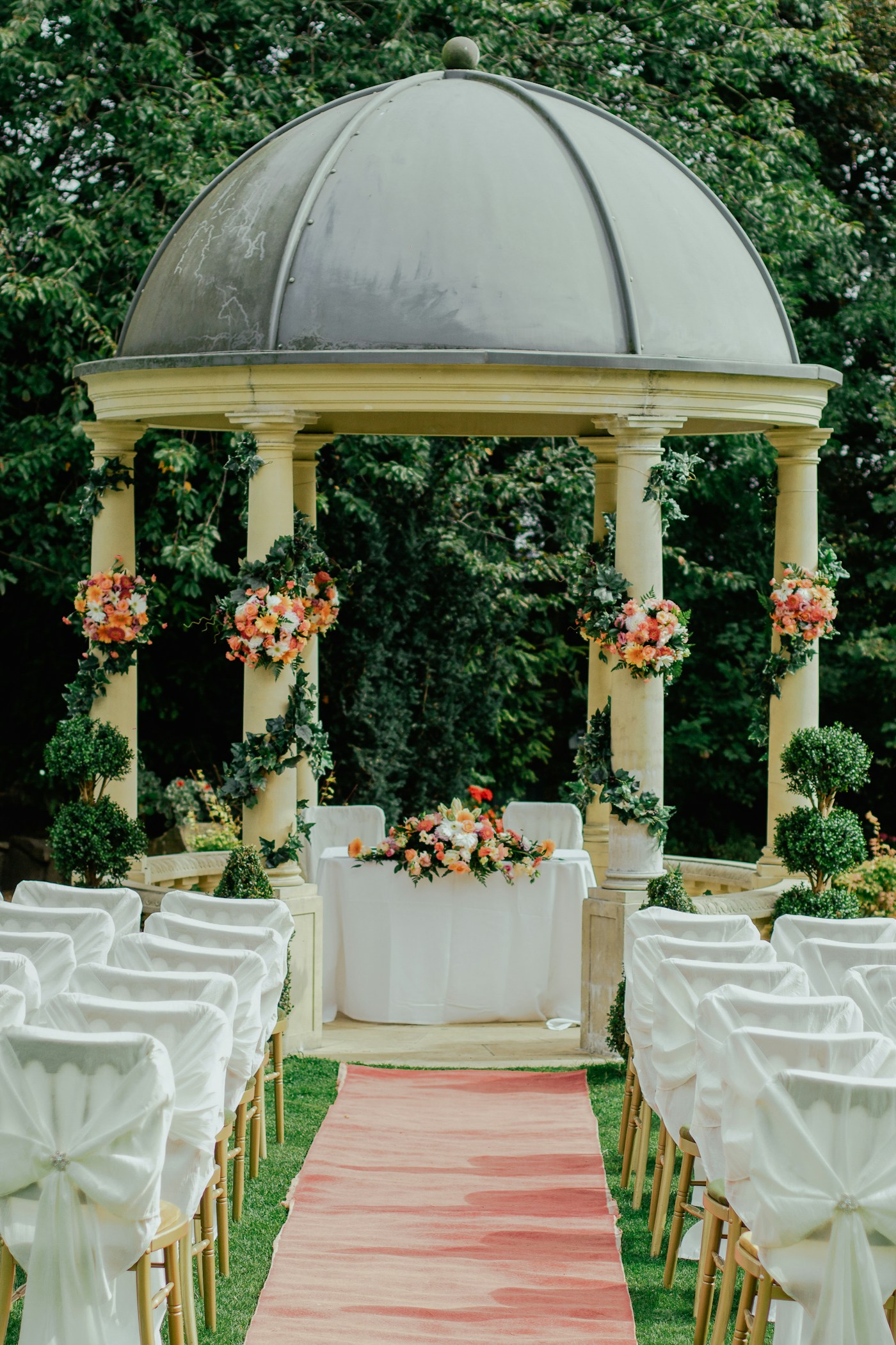 A garden ceremony setting with flowers and a soft pink aisle